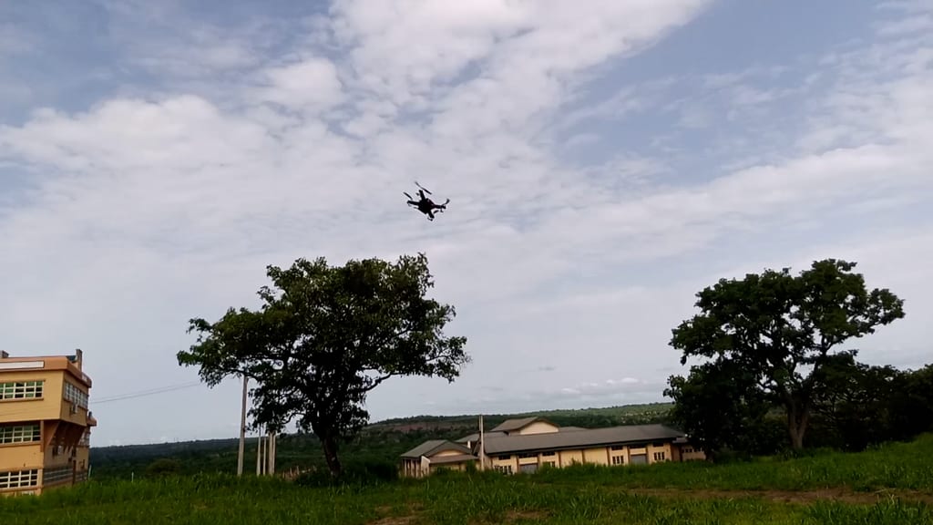 The project quadcopter flying above a grassy campus field